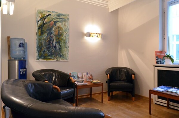 Wartezimmer mit Ledersesseln, Wasserautomat, Zeitschriften und moderner Kunst an der Wand.